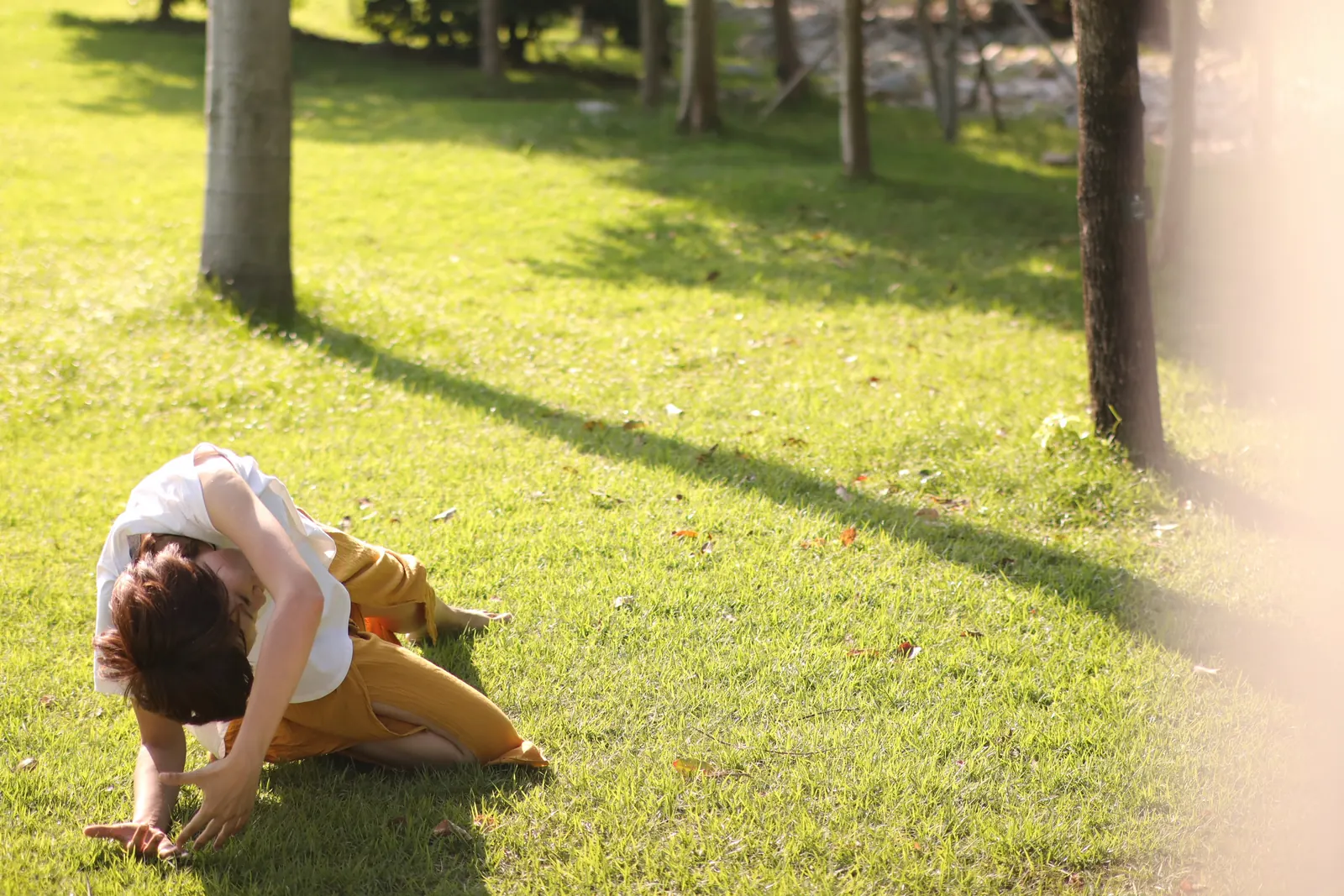 Sarah in a graceful seated stretch on sunlit grass among trees